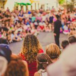 Artistas se apresentam em um espaço público enquanto um público diversificado acompanha a performance.