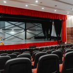 Teatro vazio com cortinas vermelhas abertas e palco iluminado, pronto para uma apresentação