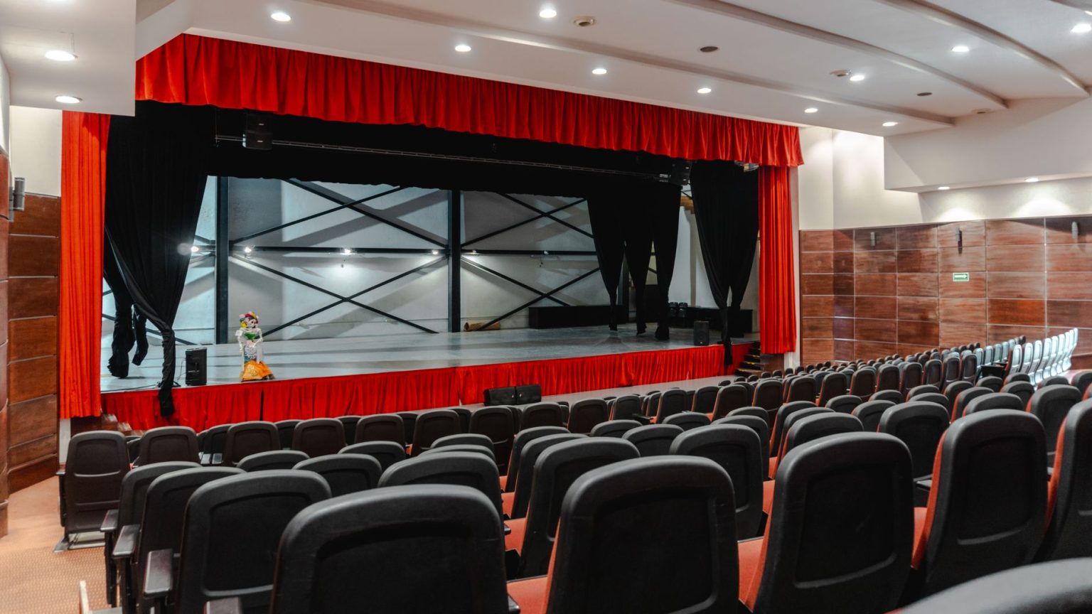 Teatro vazio com cortinas vermelhas abertas e palco iluminado, pronto para uma apresentação