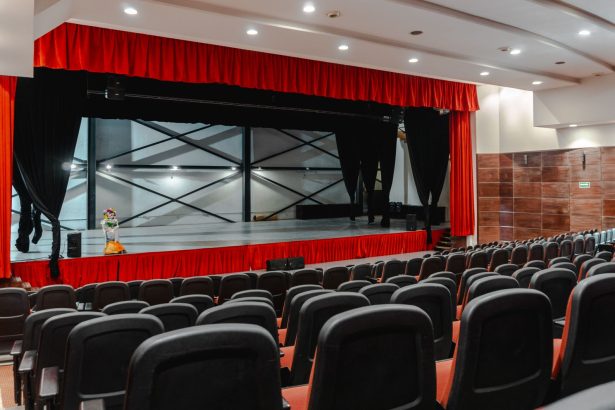 Teatro vazio com cortinas vermelhas abertas e palco iluminado, pronto para uma apresentação