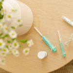 Caneta injetora, seringas e outros itens de cuidado médico dispostos sobre uma mesa de madeira.